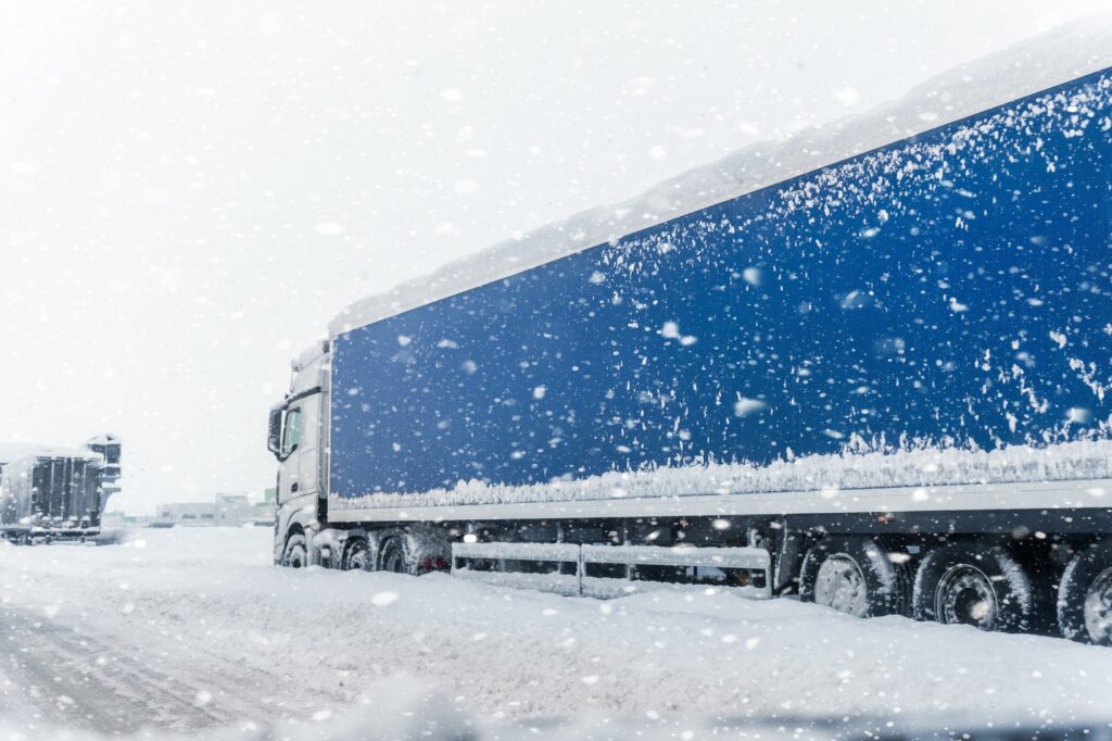 Big commercial semi-trailer truck trapped in snow drift on closed highway road at heavy snow storm